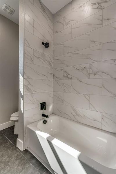 Bathroom with tiled shower / bath, tile patterned flooring, and toilet