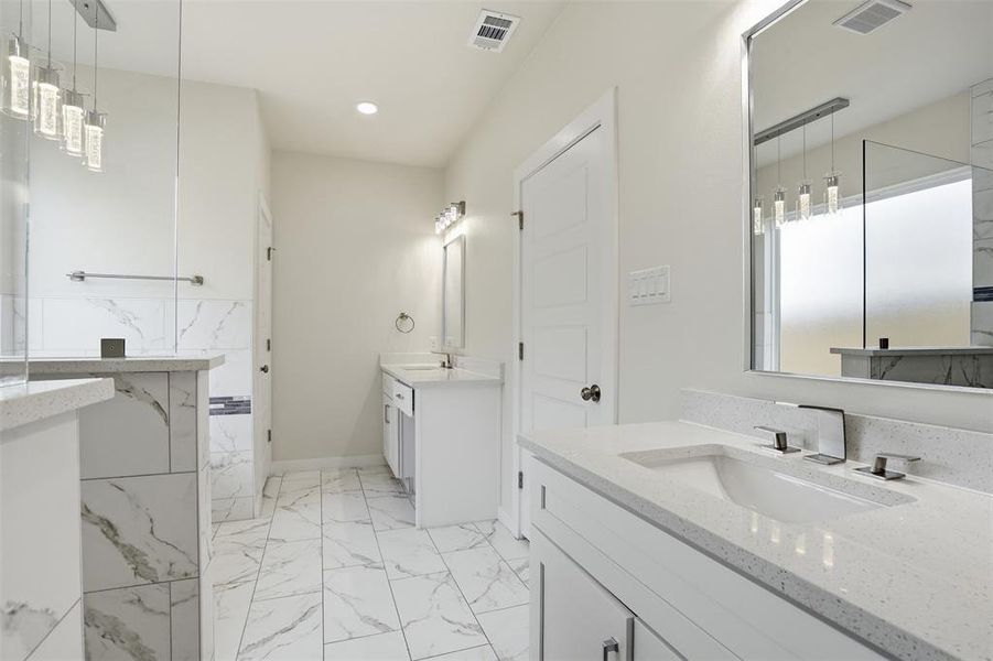 Spacious bathroom featuring white stone-finish flooring, dual vanities with integrated sinks, and quartz countertops