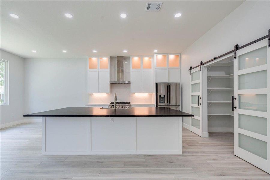 Kitchen showcasing lighted cabinets, range hood, stainless steel, and modern barn door pantry