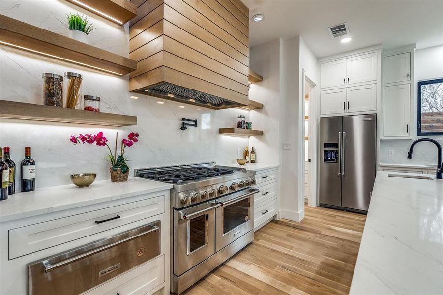 Kitchen featuring light stone countertops, custom range hood, stainless steel appliances, sink, and white cabinets