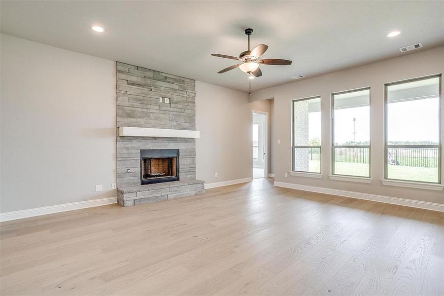 Unfurnished living room with ceiling fan, a stone fireplace, and light hardwood / wood-style floors