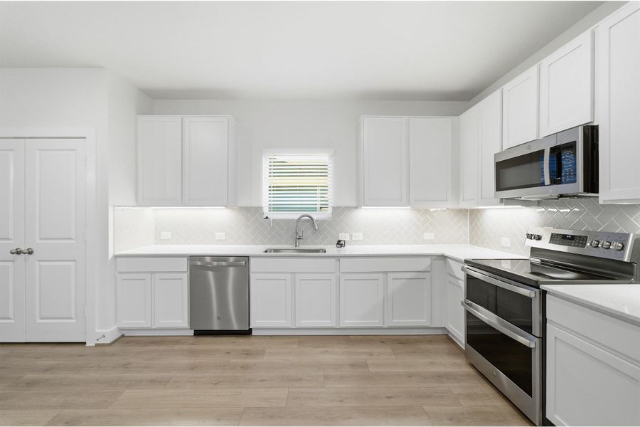 Kitchen with stainless steel appliances, white cabinets, backsplash, and light wood-type flooring