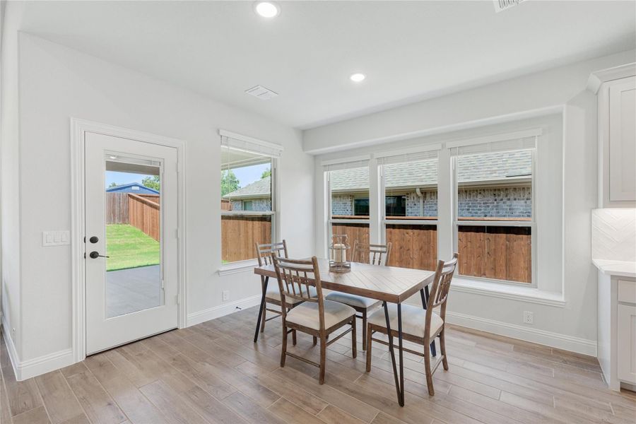 Bright dining area with wood table, four chairs, large windows, and glass door to backyard Bright dining area with wood table, four chairs, large windows, and glass door to backyard