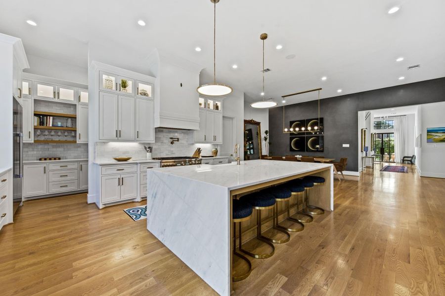 Alternate view of the chef’s kitchen showcasing custom cabinetry, premium appliances, and exceptional storage throughout. Highlights include recessed lighting, under-cabinet lighting, wide-plank hardwood flooring, and a seamless flow into dining and living spaces—designed for both everyday living and entertaining.