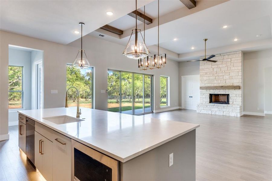 Kitchen with light wood finished floors, stainless steel appliances, hanging light fixtures, a fireplace, and beamed ceiling Kitchen with light wood finished floors, stainless steel appliances, hanging light fixtures, a fireplace, and beamed ceiling