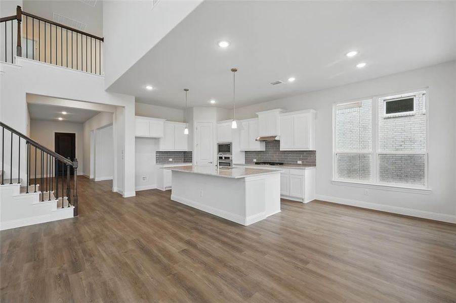 Kitchen with light countertops, white cabinetry, appliances with stainless steel finishes, under cabinet range hood, and dark wood-style flooring