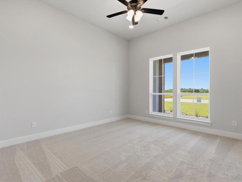 Spacious room with light neutral wall tones, plush carpet flooring, two large windows, a ceiling fan with integrated lighting, and white baseboards