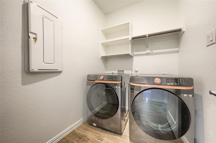 Washroom with a textured wall, wood finished floors, electric panel, and washer and dryer Washroom with a textured wall, wood finished floors, electric panel, and washer and dryer