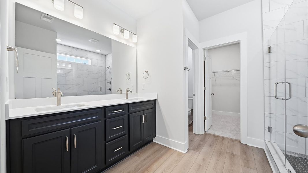 Memorable mornings begin in this elegant primary bathroom with walk-in shower and double vanity by DRB Homes