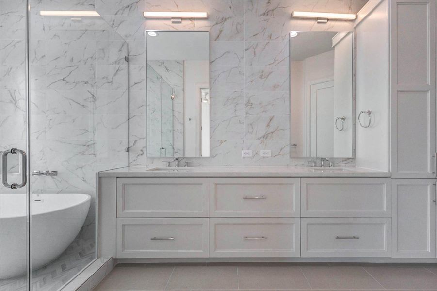 Spa-inspired primary bath featuring a double vanity with Quartz countertops, undermount sinks, sleek chrome fixtures, and full-height mirrors with modern lighting. Marble-look tile extends across the walls for a luxurious finish, while custom cabinetry offers generous storage consistent with the home’s elevated design.