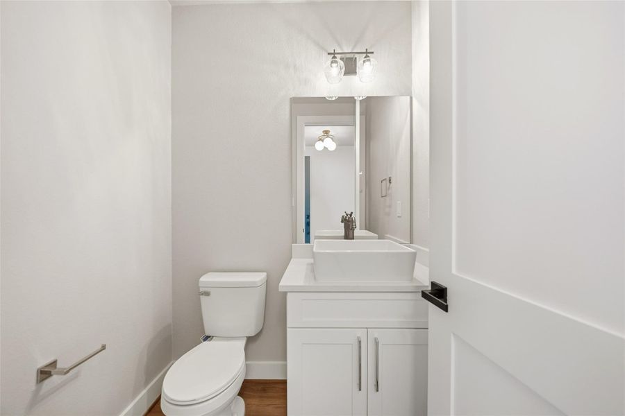 This is a modern, compact bathroom featuring a white vanity with a vessel sink, a large mirror, a toilet, and elegant light fixtures, creating a clean and bright atmosphere.