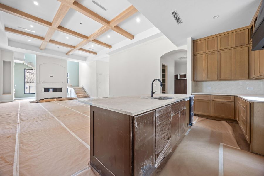 Spacious kitchen island with an integrated sink and matte black faucet, surrounded by wood cabinetry, light countertops, and a white tile backsplash