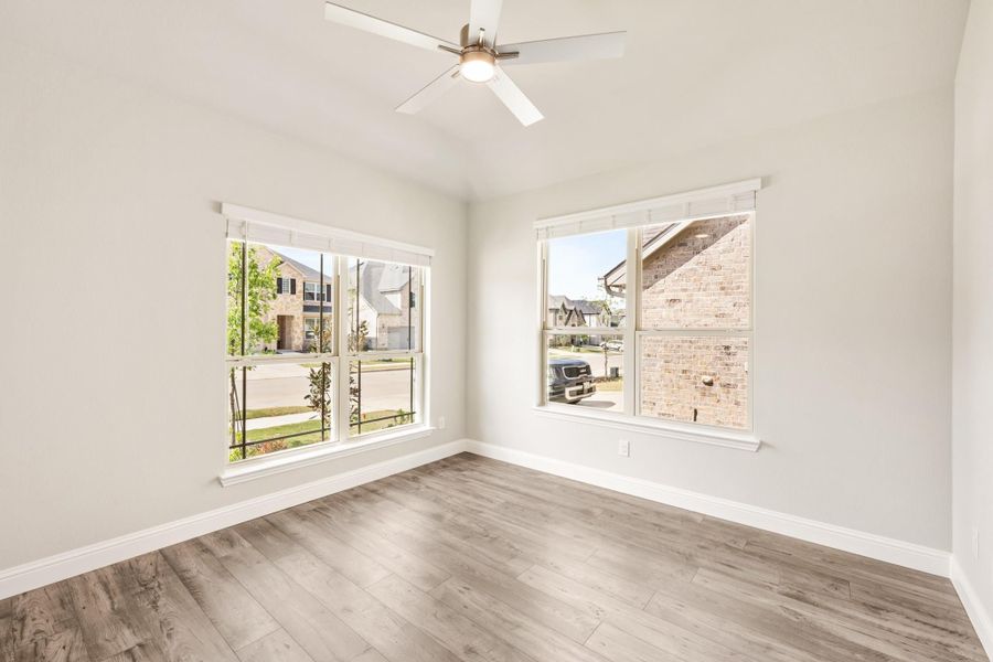 Empty room with light wood floors, ceiling fan, and two large windows overlooking a neighborhood street