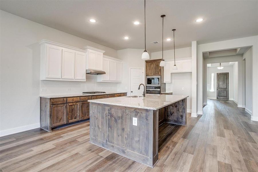 Kitchen featuring appliances with stainless steel finishes, decorative light fixtures, an island with sink, and white cabinets