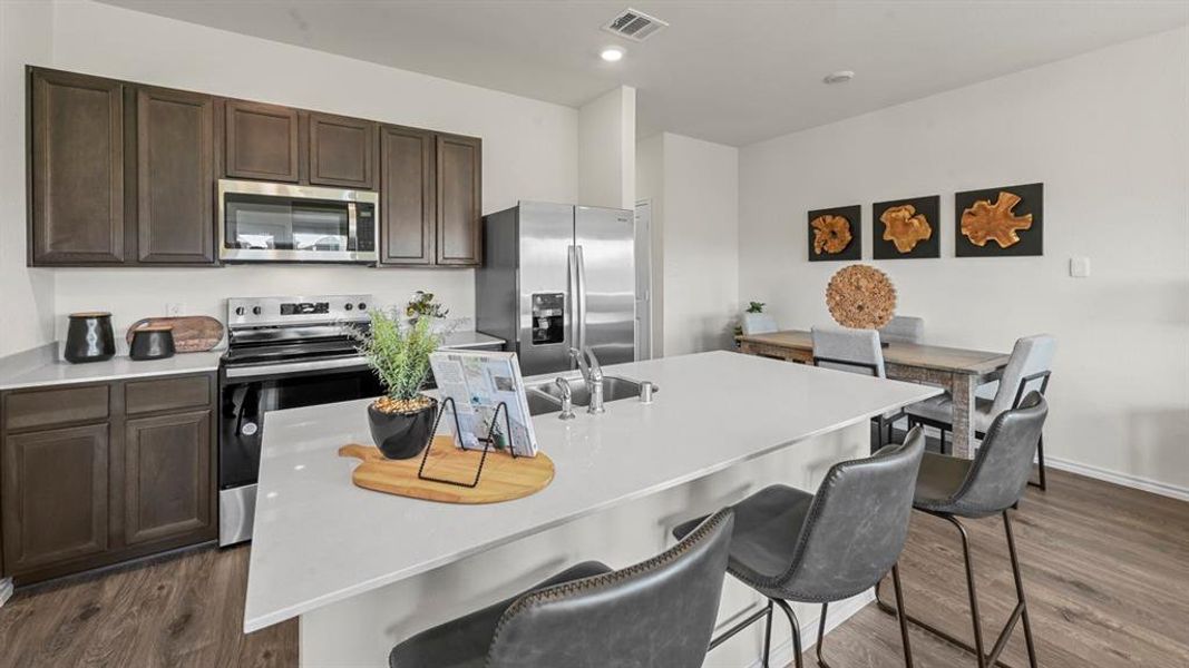 Kitchen with stainless steel appliances, dark brown cabinetry, a breakfast bar, an island with sink, and dark wood-style floors