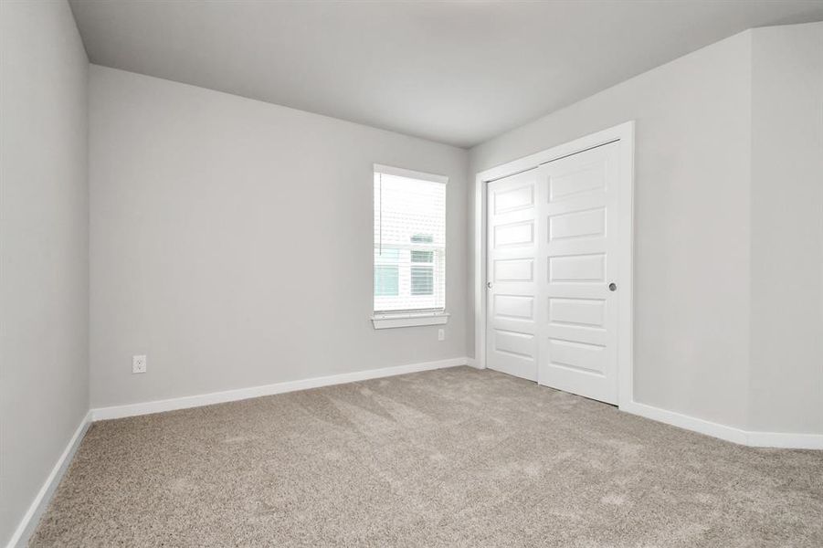 Secondary bedrooms feature elegant 5-panel doors with sleek, contemporary hardware that adds a touch of sophistication. Sink your feet into the plush, fluffy carpet that invites comfort and warmth. Large windows flood the space with an abundance of natural light, framed by privacy blinds that offer the perfect balance between openness and seclusion. Sample photo of completed home with similar floor plan. As-built interior colors and selections may vary.