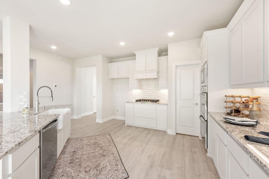 Bright kitchen with white cabinets, granite countertops, stainless steel appliances, and light wood floors