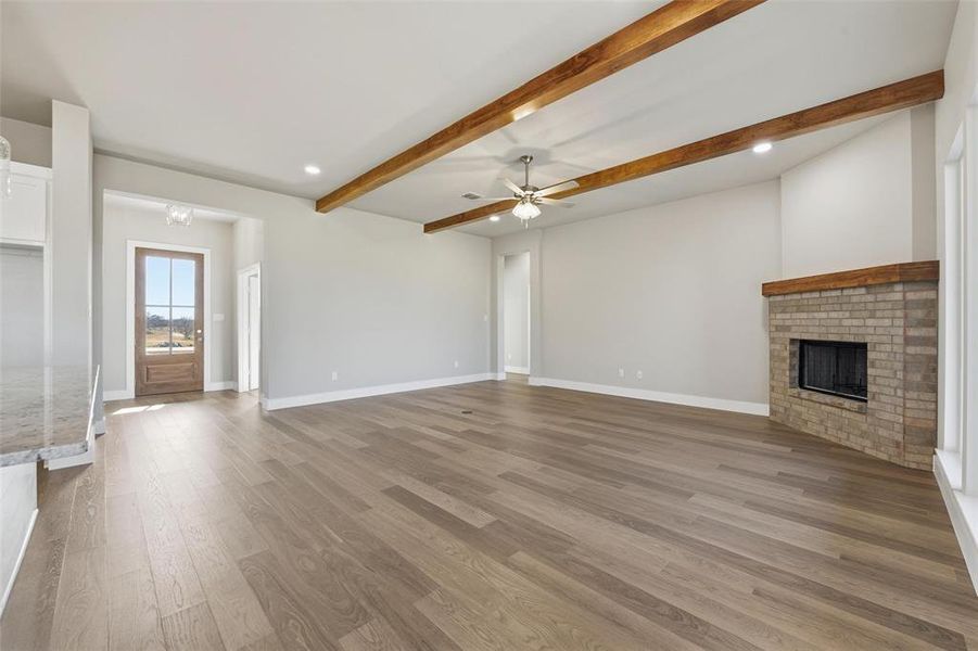Unfurnished living room with a fireplace, beam ceiling, recessed lighting, light wood finished floors, and a ceiling fan
