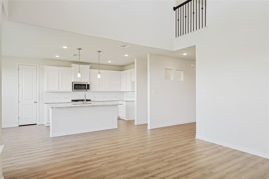 Kitchen with a kitchen island with sink, light stone countertops, decorative light fixtures, white cabinetry, and light hardwood / wood-style floors