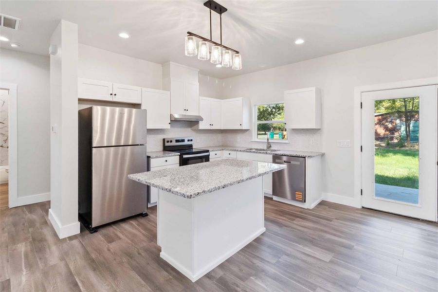 Kitchen featuring appliances with stainless steel finishes, white cabinetry, pendant lighting, light stone counters, and a kitchen island