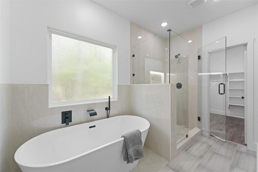 Contemporary bathroom featuring a freestanding soaking tub with matte black fixtures, a spacious glass-enclosed shower with tiled walls and pebble flooring, and large format floor tiling Contemporary bathroom featuring a freestanding soaking tub with matte black fixtures, a spacious glass-enclosed shower with tiled walls and pebble flooring, and large format floor tiling