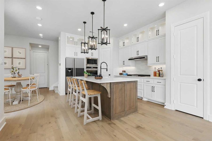 Kitchen featuring glass insert cabinets, a kitchen bar, white cabinets, a kitchen island with sink, and recessed lighting