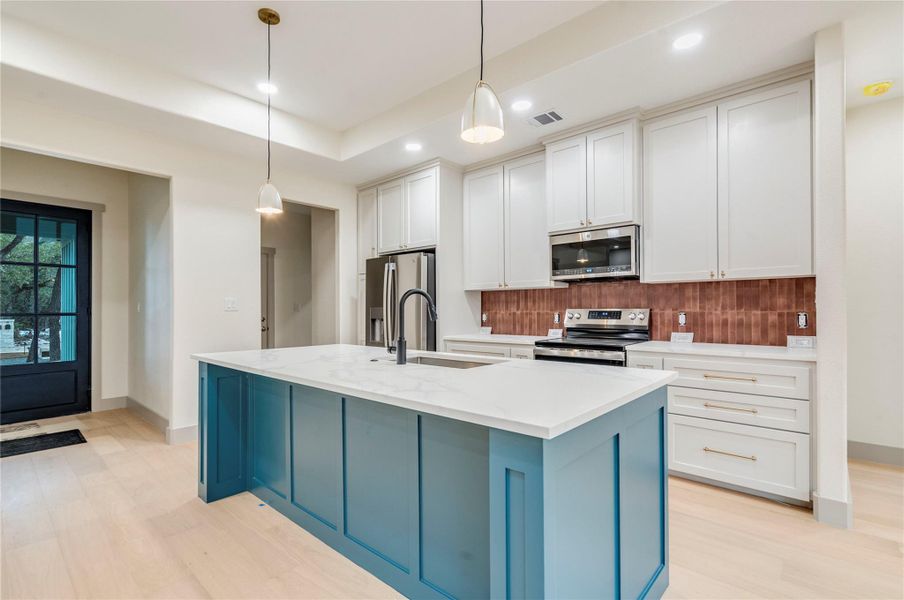 Kitchen featuring blue cabinets, appliances with stainless steel finishes, hanging light fixtures, white cabinetry, and decorative backsplash