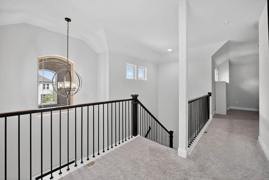 Upper-level hallway featuring a vaulted ceiling and a globe chandelier