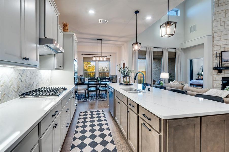 Kitchen featuring pendant lighting, light stone counters, an island with sink, high vaulted ceiling, and open floor plan
