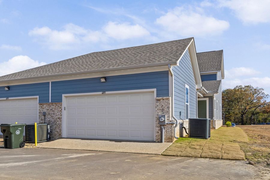 View of home's exterior with stone siding, roof with shingles, a garage, and driveway