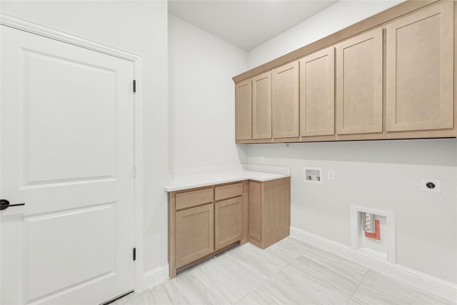 Laundry room with light wood upper cabinets, lower cabinet with white countertop, and washer and dryer hookups on tile floor.