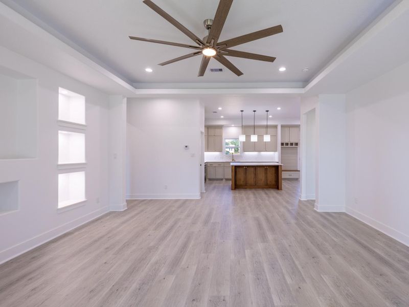 This photo showcases a spacious open-concept living and kitchen area with modern wood flooring, a large ceiling fan, and recessed lighting. The kitchen features an island with pendant lights, ample cabinetry, and a stylish design, perfect for entertaining.