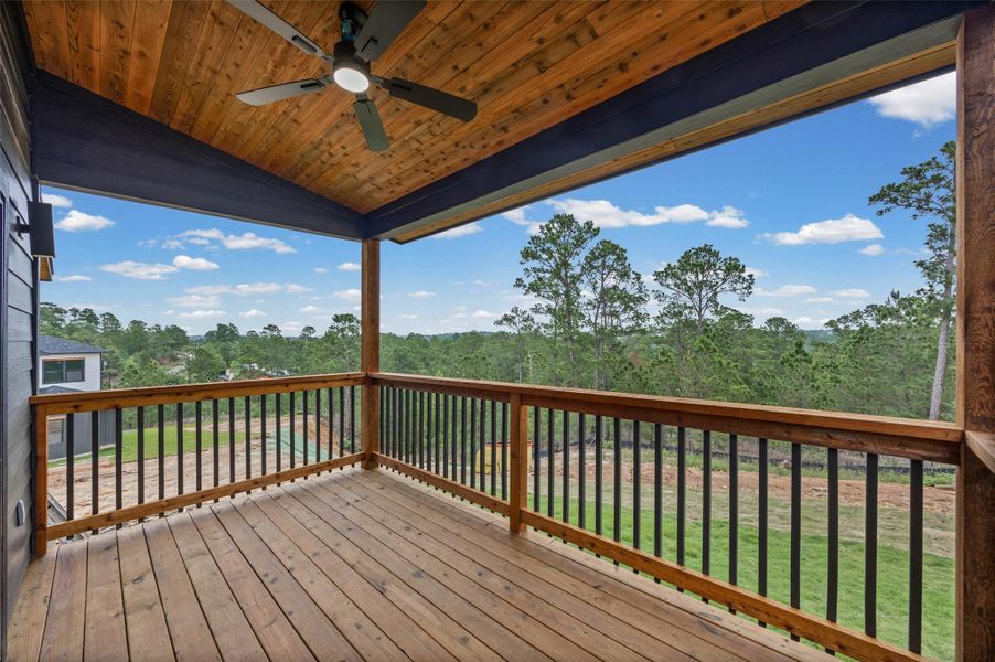 Covered outdoor deck featuring natural wood flooring and railing, black balusters, and a wood-paneled ceiling with a built-in ceiling fan Covered outdoor deck featuring natural wood flooring and railing, black balusters, and a wood-paneled ceiling with a built-in ceiling fan