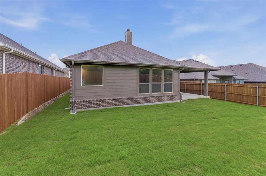 Expansive rear lawn featuring a covered patio, full privacy fencing, brick foundation, multiple windows, and a shingle roof