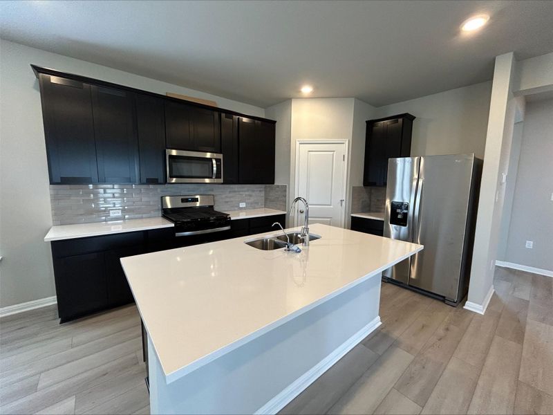Kitchen with dark cabinetry, stainless steel appliances, a kitchen island with sink, decorative backsplash, and recessed lighting Kitchen with dark cabinetry, stainless steel appliances, a kitchen island with sink, decorative backsplash, and recessed lighting