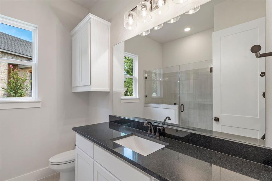 Bathroom featuring toilet, vanity, and an enclosed shower