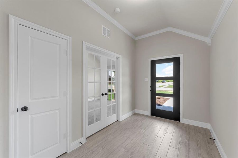 Entryway with ornamental molding, french doors, lofted ceiling, and light wood-type flooring