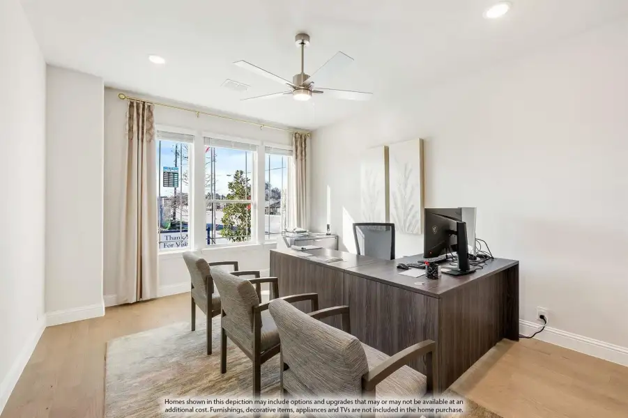 Home office with dark wood desk, ceiling fan, hardwood floors, and two guest chairs near large windows