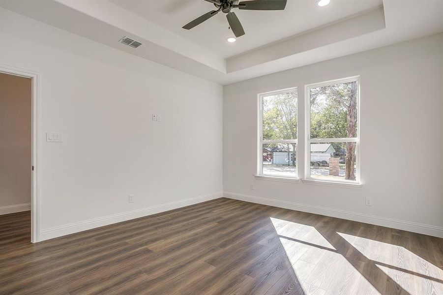 Empty room with a tray ceiling, dark wood-type flooring, recessed lighting, and ceiling fan