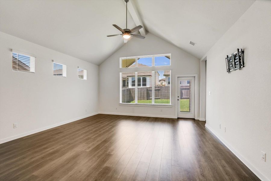 Spacious living area featuring a vaulted ceiling with a ceiling fan, wood-finish flooring, multiple windows, and a glass-paneled door