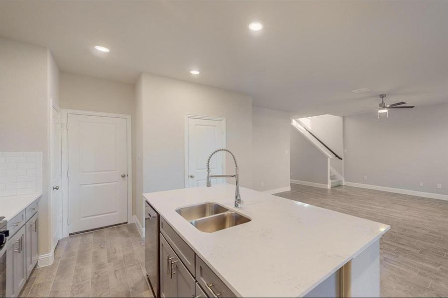 Kitchen with stainless steel dishwasher, ceiling fan, sink, light hardwood / wood-style floors, and an island with sink