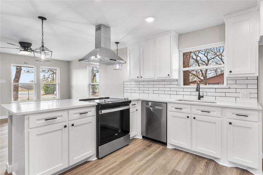 Kitchen featuring stainless steel appliances, island exhaust hood, white cabinets, a peninsula, and hanging light fixtures