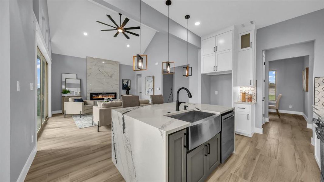 Kitchen with white cabinets, pendant lighting, light stone counters, a fireplace, and a kitchen island with sink