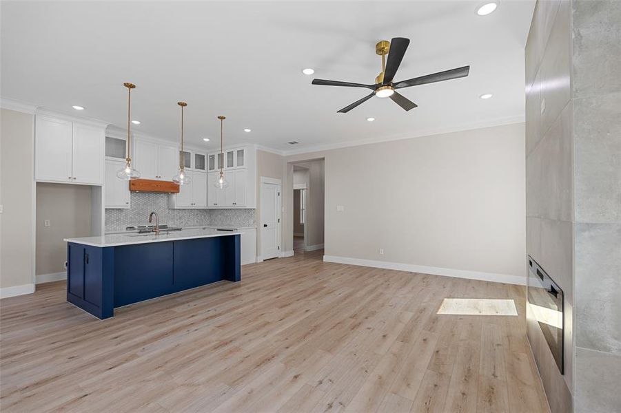 Kitchen featuring light wood-type flooring, sink, white cabinets, decorative light fixtures, and ceiling fan