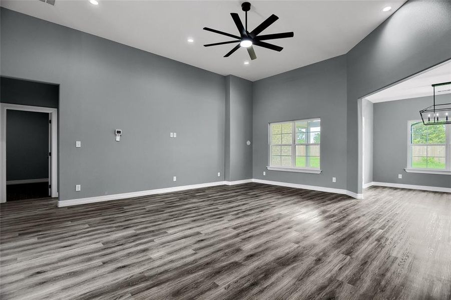 Empty room with a high ceiling, ceiling fan with notable chandelier, and wood-type flooring