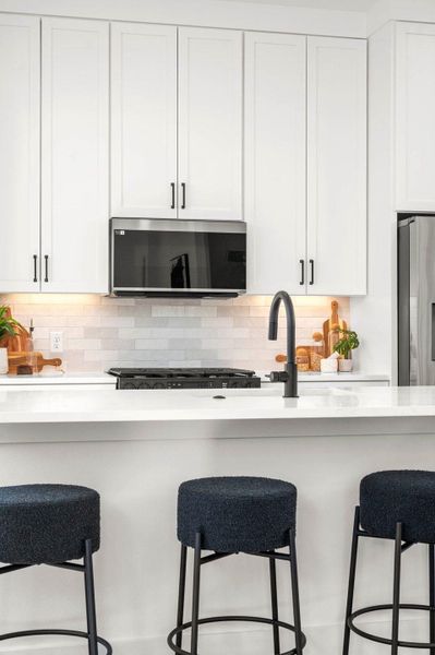 Kitchen featuring white cabinets, stainless steel appliances, a breakfast bar area, and decorative backsplash Kitchen featuring white cabinets, stainless steel appliances, a breakfast bar area, and decorative backsplash