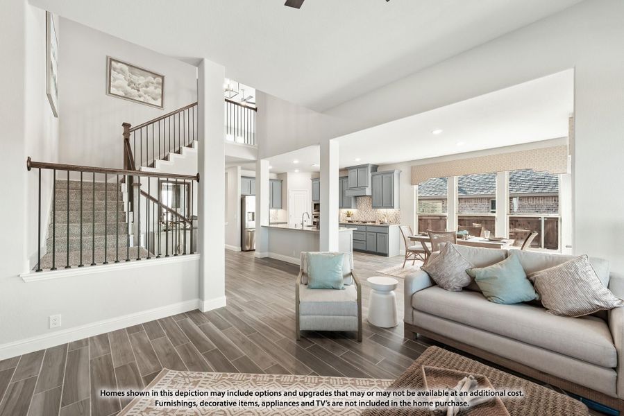 Open-concept living room with wood-look tile floors, staircase, and kitchen visible in background Open-concept living room with wood-look tile floors, staircase, and kitchen visible in background