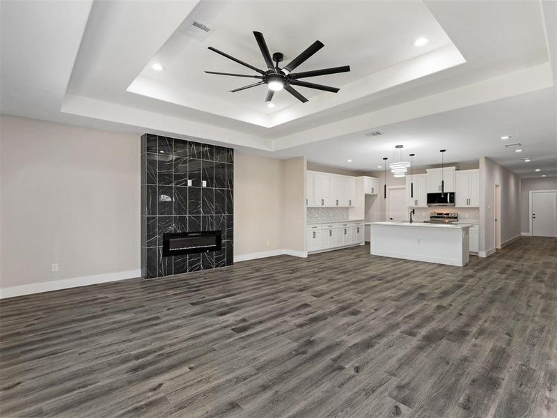 Unfurnished living room with ceiling fan, dark hardwood / wood-style floors, a raised ceiling, and a premium fireplace