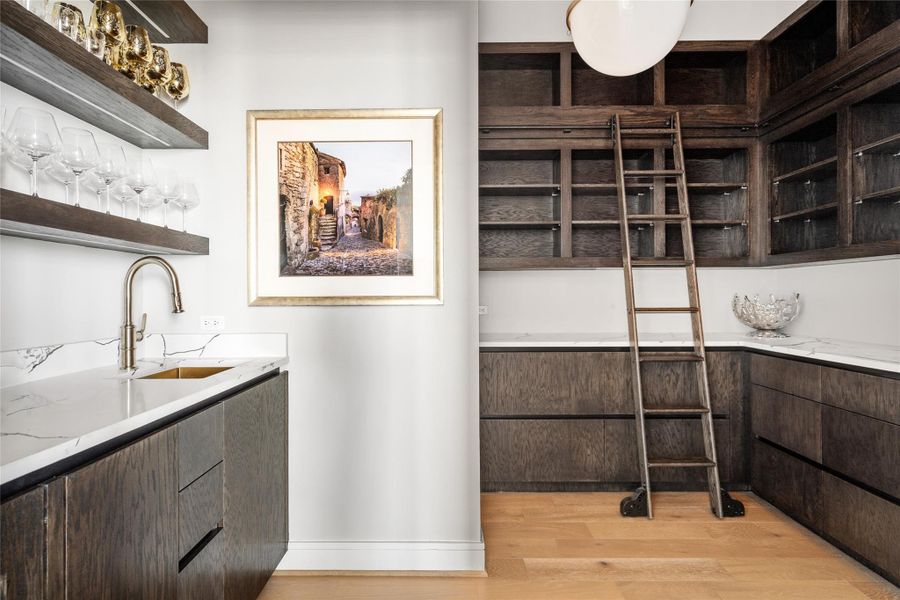 Elegant in-home bar featuring custom cabinetry, integrated pantry space, ice maker and U-Line beverage refrigerator, and a rolling ladder for both style and functionality.