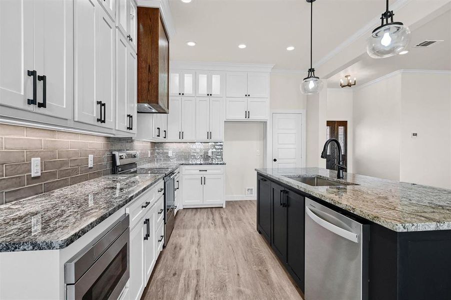 Kitchen with sink, appliances with stainless steel finishes, light hardwood / wood-style flooring, hanging light fixtures, and white cabinets